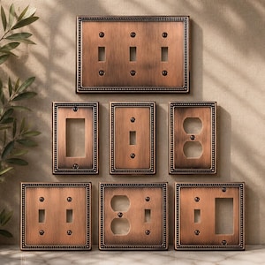 May include: A collection of seven rectangular wall plates with a brushed copper finish and a beaded border. The set includes various configurations for light switches and electrical outlets, each secured with matching screws in the corners.