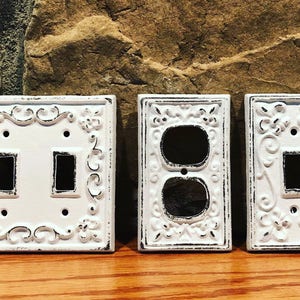 May include: Three white decorative light switch covers with ornate designs. The covers are made of cast iron and have a distressed finish.