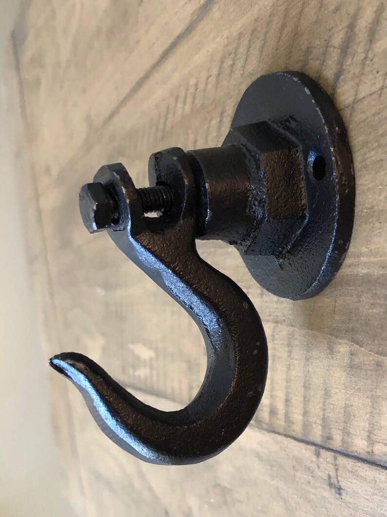 May include: Black metal hook with a round base and a screw. The hook is attached to a wooden surface.