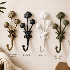 May include: Four wall hooks shaped like mushroom clusters, available in vintage gold, black, white, and Italian olive finishes. Each hook features three mushroom caps on stems branching from a central base with two screw holes for mounting.