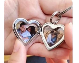 May include: A silver heart-shaped locket keychain, open to reveal two small photographs. The locket is held open, displaying the pictures of a couple. The keychain is a romantic keepsake.