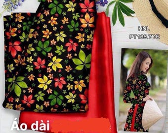 May include: Red and black fabric with a pattern of green, yellow, and red leaves. The fabric is folded in half and the text "Áo dài" is visible in the bottom left corner. The text "HNL PT165.7DE" is visible in the top right corner.