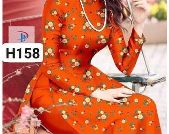 May include: A woman wearing a traditional orange and white floral patterned dress with a high collar and long sleeves. The dress has a split in the front and the woman is wearing a pearl necklace. The text "H158" and "Áo dài Huế" is visible in the image.