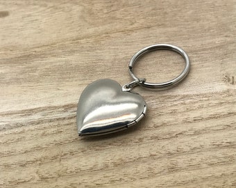 May include: A silver heart-shaped locket keychain with a hinged opening. The locket is attached to a silver key ring.