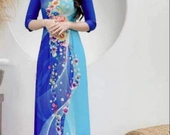 May include: A woman wearing a long blue and light blue dress with a floral pattern. The dress has a round neckline and three-quarter sleeves. The dress is made of a soft, flowing fabric.