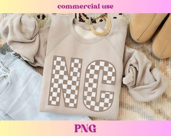 May include: A light brown sweatshirt with the letters NC in a checkered pattern. The letters are large and take up most of the front of the sweatshirt.