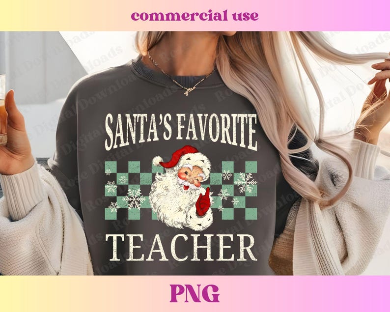 Puede incluir: Una sudadera gris con el texto "SANTA'S FAVORITE TEACHER" en blanco con un aspecto vintage desgastado. Una imagen de dibujos animados de Pap&aacute; Noel con un gorro rojo y barba blanca est&aacute; en el centro del texto.