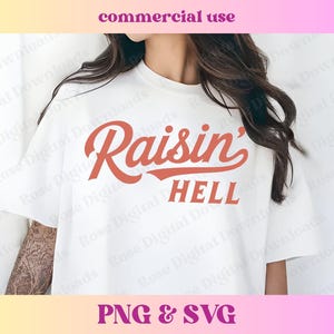Puede incluir: Una camiseta blanca con el texto "Raisin' Hell" en una fuente roja y cursiva. El texto está en una camiseta blanca que lleva una persona.