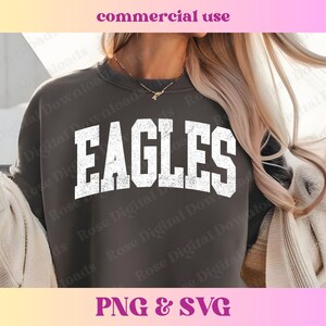 以下が含まれることがあります： 暗いグレーのトレーナーに、白で「EAGLES」という文字がヴィンテージ風のダメージ加工でプリントされています。
