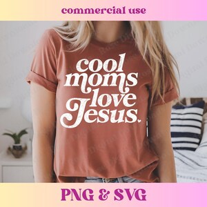 May include: A rust-colored t-shirt with the text "Cool Moms Love Jesus" in white lettering. The shirt has a relaxed fit and a crew neck.
