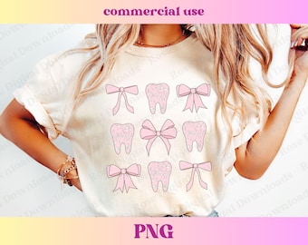 May include: A white t-shirt with a pink design of teeth and bows. The teeth are decorated with small pink flowers. The bows are tied with a pink ribbon.