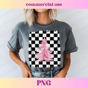 Puede incluir: Una camiseta gris con un diseño de árbol rosa acuarela sobre un fondo a cuadros blanco y negro. El diseño tiene un aspecto desgastado.