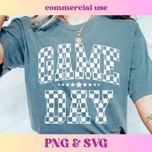 May include: A blue t-shirt with the text "GAME DAY" in white checkered letters. The letters are outlined in black and have a distressed look.