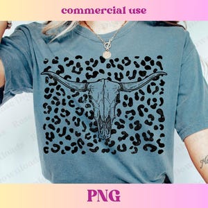 May include: A blue t-shirt with a black and white graphic of a cow skull with horns on a leopard print background.