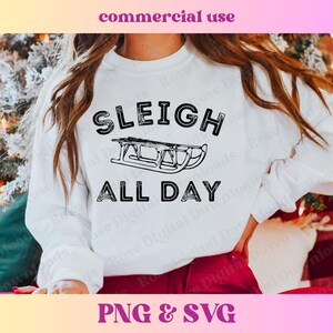 以下が含まれることがあります： 黒い文字で「Sleigh All Day」と書かれた白いスウェットシャツ。黒と白のそりのイラストが描かれている。