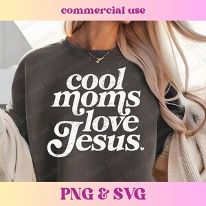 May include: A dark gray sweatshirt with the text "cool moms love Jesus." in white, retro-style lettering. The sweatshirt is worn by a person with long blonde hair.