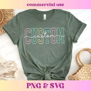 Peut inclure: Un t-shirt vert avec le mot "CUSTOM" en lettres majuscules colorées. Le mot "custom" est écrit en cursive sous les lettres majuscules.