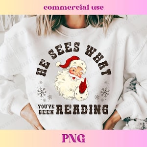 Puede incluir: Sudadera blanca con una ilustración vintage de Papá Noel y el texto "He Sees What You've Been Reading".