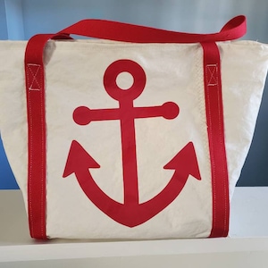 May include: White tote bag with red anchor graphic and red handles. The bag is made of a durable material and features a large red anchor design on the front. The red handles are securely attached to the bag, making it easy to carry.