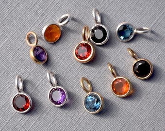 May include: Ten silver and gold charms with different colored gemstones. The charms feature round gemstones in red, orange, blue, purple, and black.