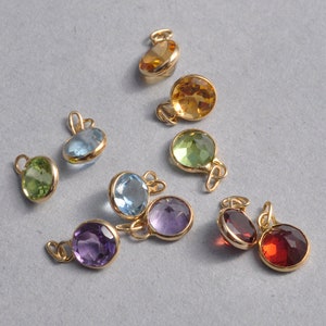 May include: Assortment of gemstone charms in various colors, including green, blue, red, orange, and purple. Each charm features a round gemstone set in a gold setting with a loop for attaching to a necklace or bracelet.