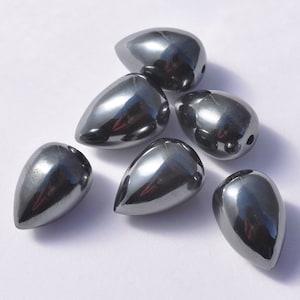 May include: Six black teardrop-shaped hematite beads. The beads are smooth and shiny.