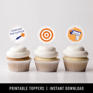 May include: Printable cupcake toppers featuring a target, a dart, and a toy gun. The toppers are on a white background and have a blue and orange color scheme. The text on the topper reads "Prepare for Battle".