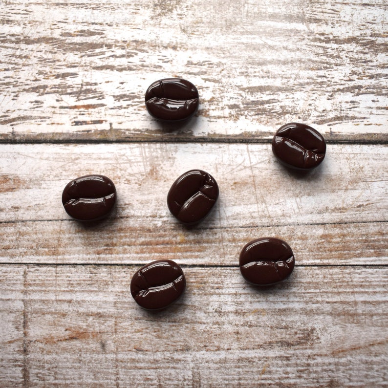 May include: Six brown coffee beans on a white wooden surface.