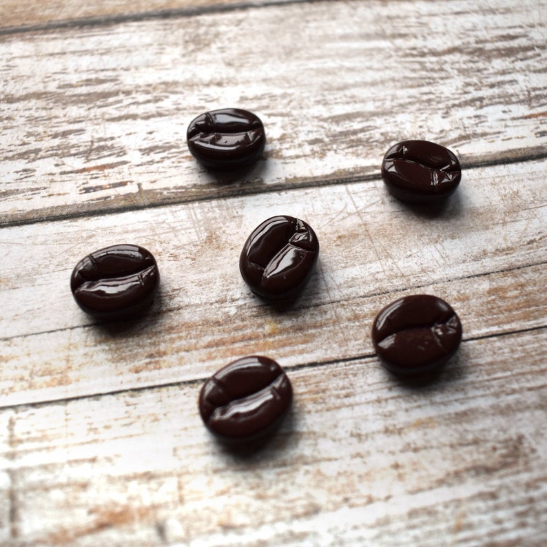 May include: Seven brown coffee bean shaped buttons on a white wooden surface.