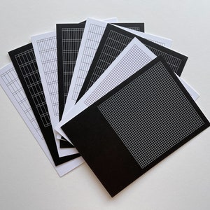May include: A set of eight black and white gridded paper sheets. The sheets are arranged in a fan shape, with the black sheets on top and the white sheets underneath.