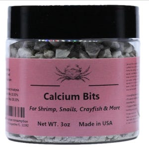May include: A clear plastic jar filled with small white calcium bits for shrimp, snails, crayfish, and more. The jar has a pink label with the text "Calcium Bits" and a small crab illustration. The label also states "Net WT. 3oz Made in USA".