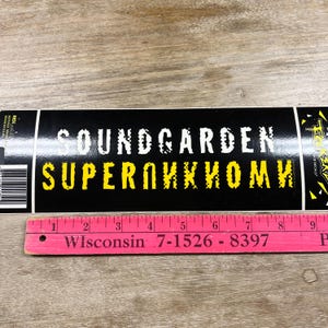 May include: A black sticker with the band name "SOUNDGARDEN" in white and "SUPERUNKNOWN" in yellow. A pink ruler with the text "Wisconsin 7-1526-8397" is at the bottom. The sticker is rectangular.