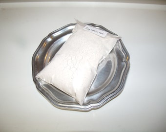 May include: A clear plastic bag filled with white powder labeled "3g White Ash" rests on a silver, scalloped-edge plate. The plate is centered on a white surface, creating a simple, clean composition.