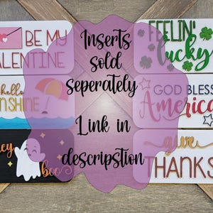 May include: A collection of 12 wooden signs with various holiday and seasonal themes. The signs feature phrases like "Happy New Year", "Be My Valentine", "Feeling Lucky", "God Bless America", "It's Fall Y'all", and "Merry Christmas".
