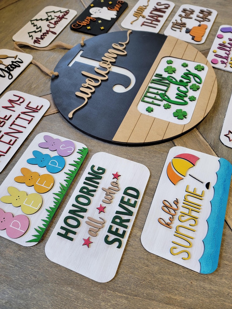 May include: A collection of wooden signs with various sayings and designs. The signs feature different colours, fonts, and styles, including a round sign with the word "Welcome" and a smaller sign with the text "Feeling Lucky".