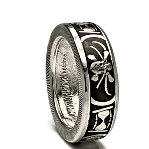 May include: A silver ring with a black design featuring an hourglass, a clover, and a skull. The ring is inscribed with "ANONYMOUS INC."