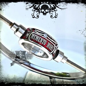 May include: A silver and red ring with the words "Memento Mori" engraved on it. The ring is attached to a silver rod.