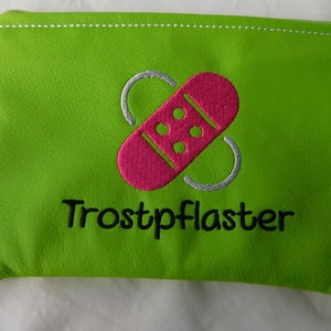 Könnte beinhalten: Eine leuchtend grüne Reißverschlusstasche mit einem weißen Reißverschluss. Die Tasche hat ein gesticktes Pflaster in Pink und Weiß mit dem Text "Trostpflaster" in Schwarz.