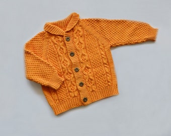 May include: A yellow knitted cardigan with a cable knit pattern and button fastening. The cardigan has a collared neckline and long sleeves.