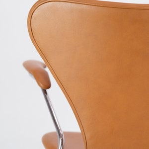 Puede incluir: Una silla de cuero marr&oacute;n con un marco cromado. La silla tiene un respaldo curvo y un asiento redondeado.