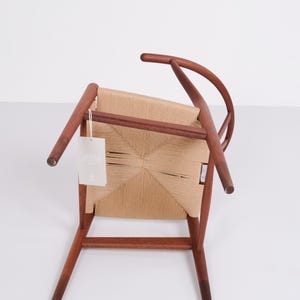 May include: A wooden chair with a woven seat and back. The chair has a curved backrest and four legs. The wood is a warm brown color, and the woven seat is a light tan. A tag hangs from the chair.