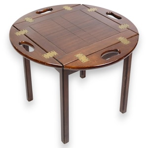May include: A round wooden table with a folding top and brass accents. The table has four legs and is made of dark wood.