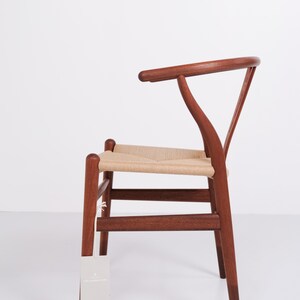 May include: A wooden chair with a woven seat and a curved backrest. The chair is made of dark brown wood and has a light beige woven seat. The chair has a tag hanging from one of the legs.
