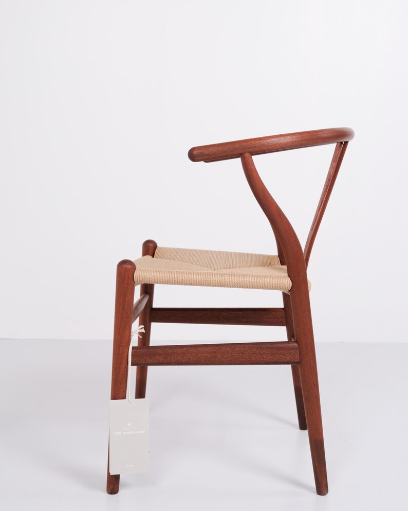 May include: A wooden chair with a woven seat and a curved backrest. The chair is made of dark brown wood and has a light beige woven seat. The chair has a tag hanging from one of the legs.