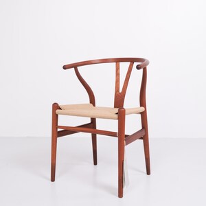 May include: A wooden chair with a curved back and woven seat. The chair is made of reddish-brown wood and has a light tan seat. The back of the chair has a distinctive Y-shape.