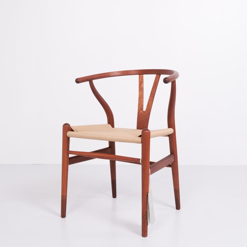 May include: A wooden chair with a curved back and woven seat. The chair is made of reddish-brown wood and has a light tan seat. The back of the chair has a distinctive Y-shape.