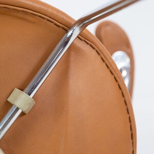 Puede incluir: Primer plano de una silla de cuero marr&oacute;n con estructura de cromo. La silla tiene una costura alrededor del borde del asiento.