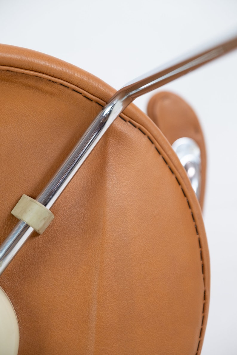 Puede incluir: Primer plano de una silla de cuero marr&oacute;n con estructura de cromo. La silla tiene una costura alrededor del borde del asiento.