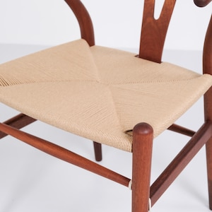 May include: A wooden chair with a woven seat. The chair features a curved back and armrests, and the seat is made of a light beige woven material. The wood is a warm brown color, and the chair has a classic, timeless design.