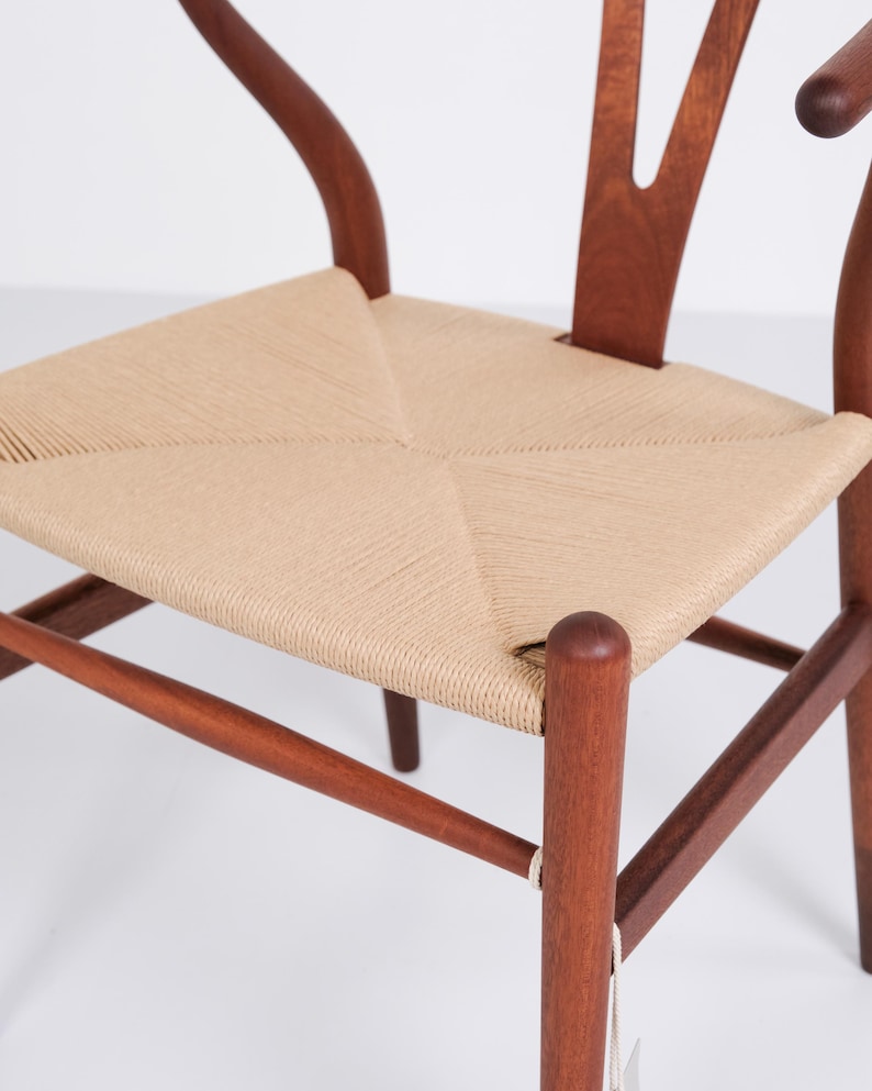May include: A wooden chair with a woven seat. The chair features a curved back and armrests, and the seat is made of a light beige woven material. The wood is a warm brown color, and the chair has a classic, timeless design.